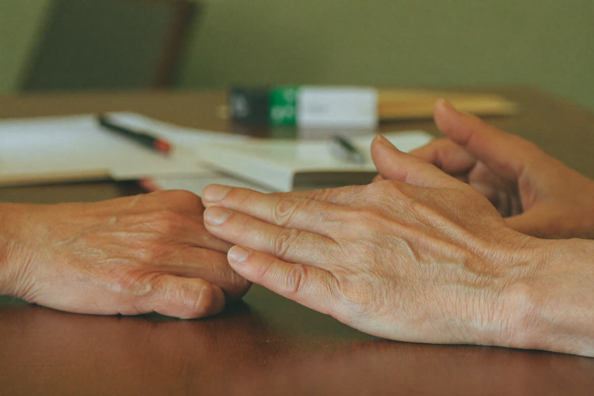 Two pairs of hands, one older and one younger, resting together on a wooden table