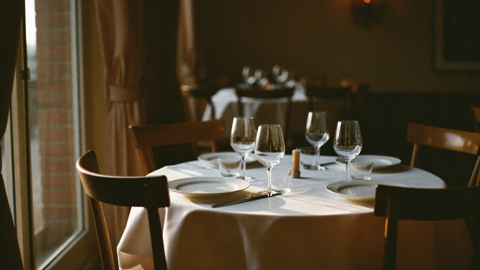 A restaurant table set for four beside a window in warm evening light