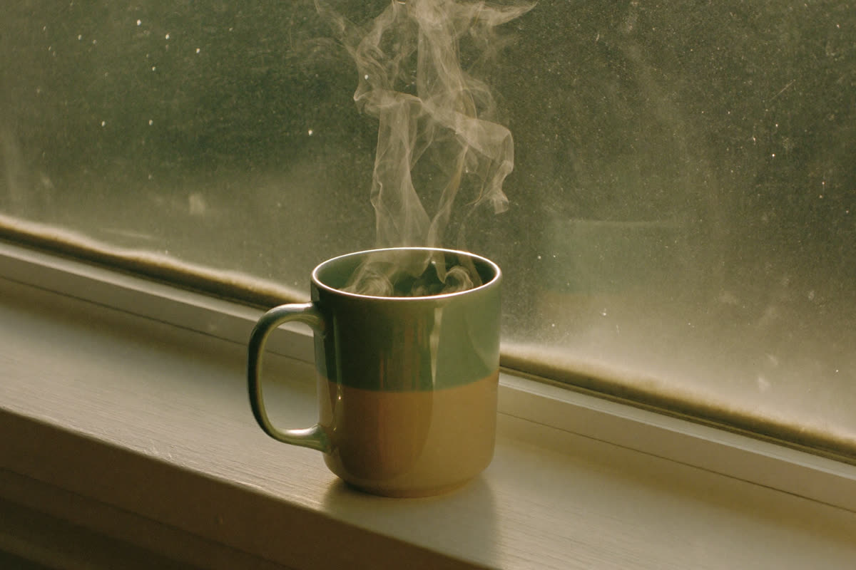 A steaming mug on a windowsill in soft morning light