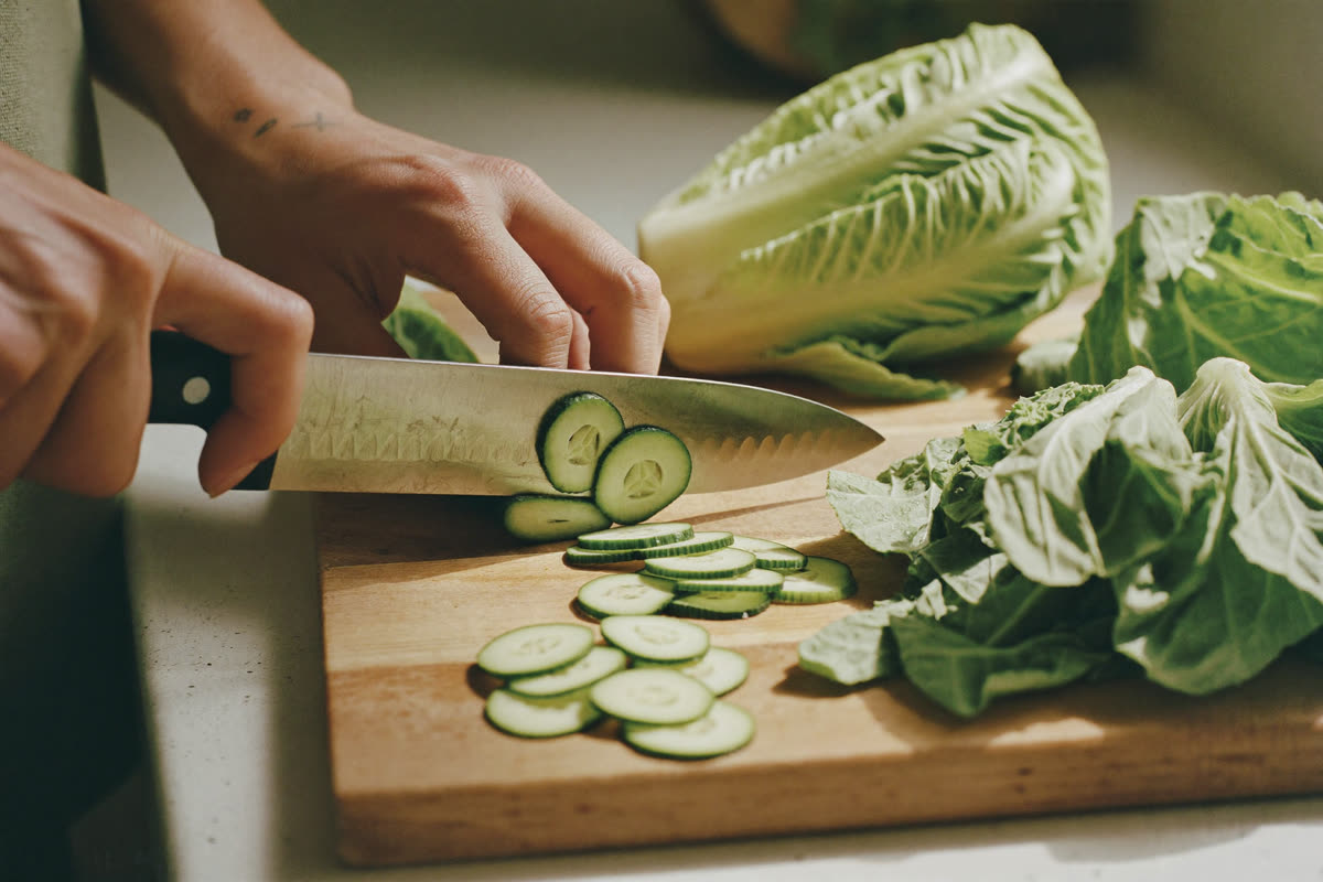 Hands slicing fresh green vegetables on a wooden board in a sunlit kitchen