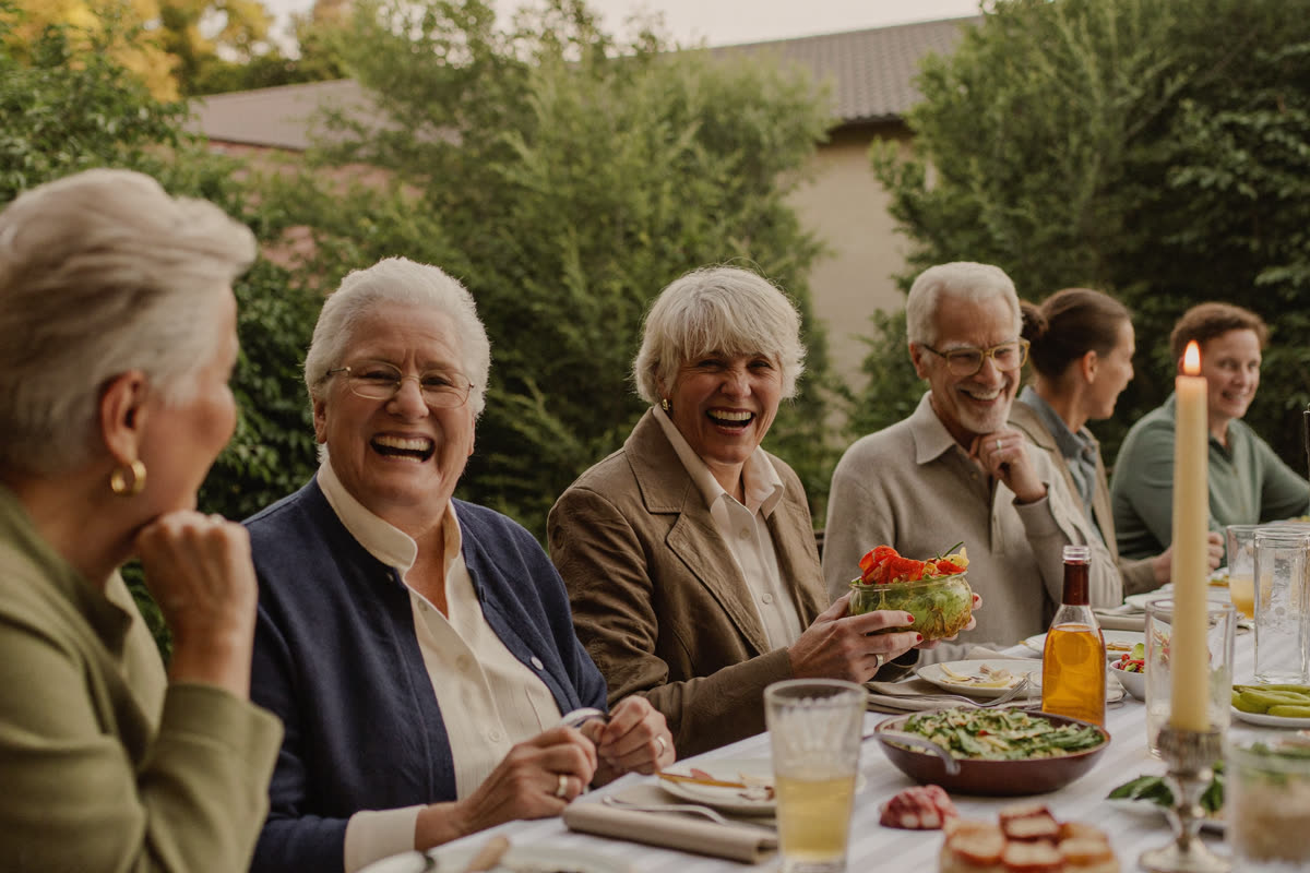 A group of older adults laughing together around an outdoor table in golden light