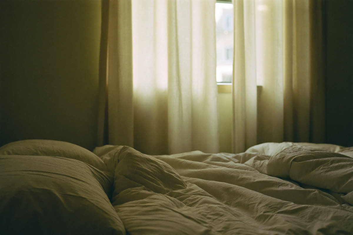 A softly lit bedroom at dawn with rumpled cream linen bedding