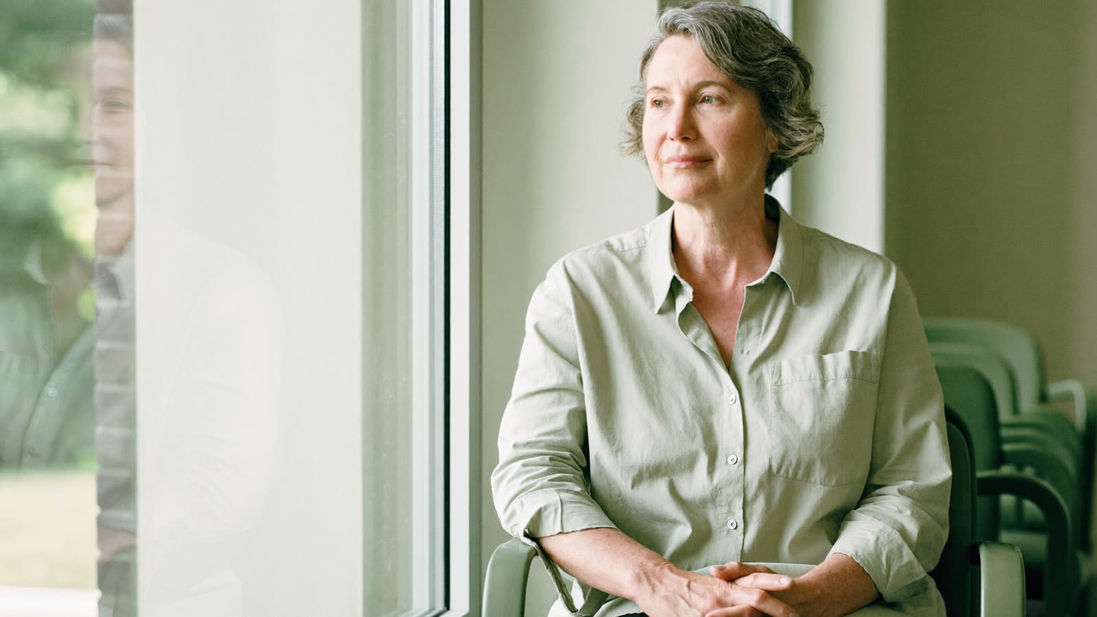 Woman in her early fifties sitting calmly by a window in a bright clinic waiting area