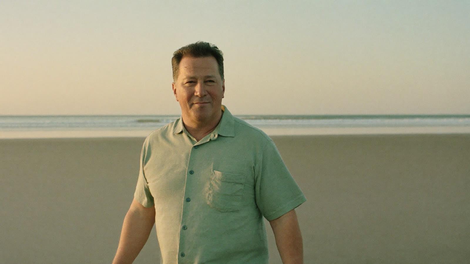 Man in his fifties walking along an open beach at sunrise, calm and rested