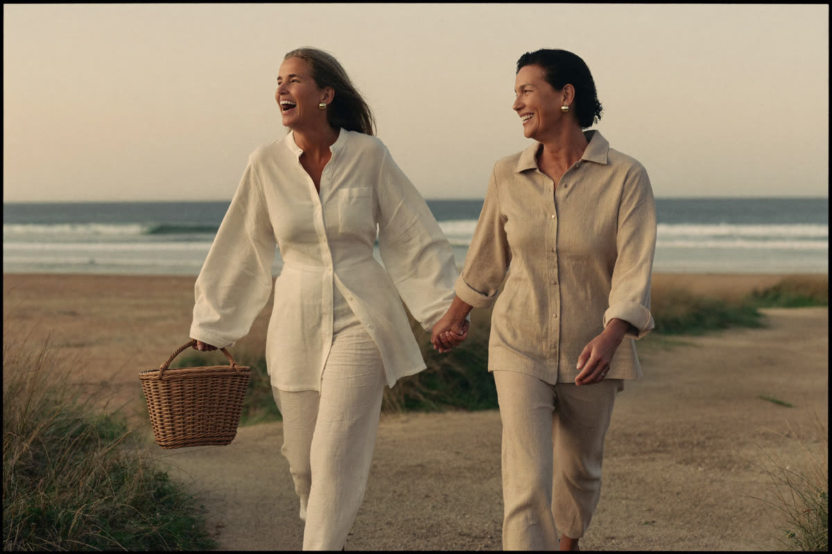 Two women laughing together while walking a beach path in soft golden light